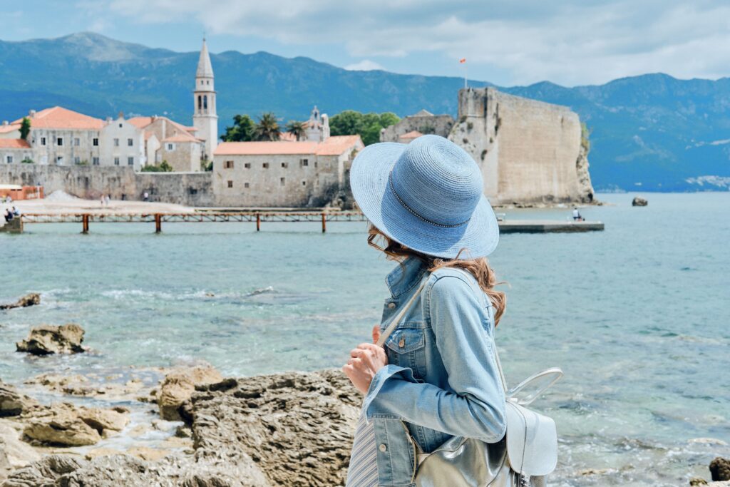 Žena v modrém klobouku stojící na pobřeží moře.